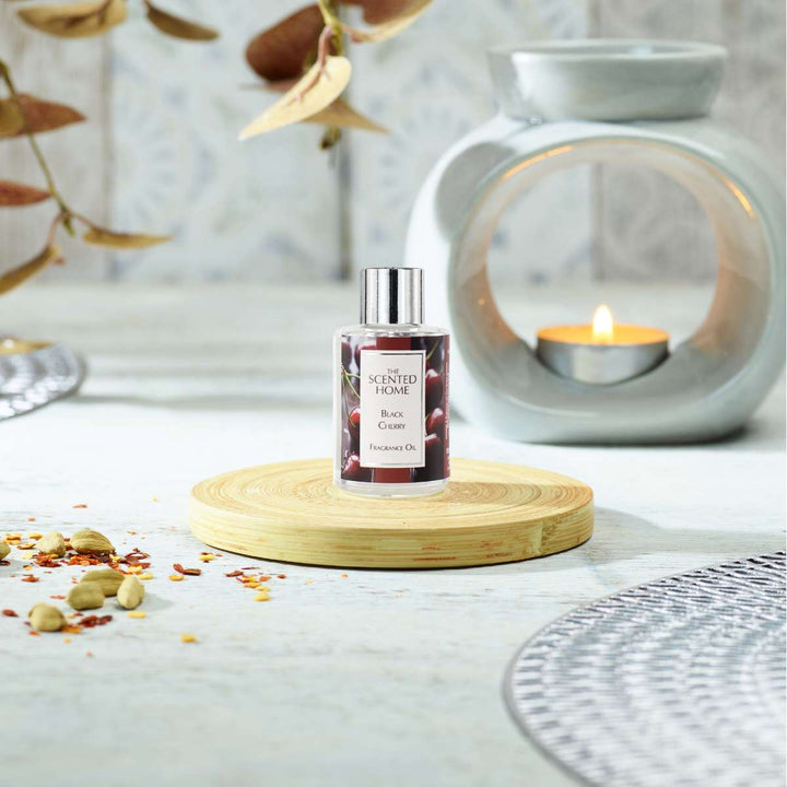 A bottle of Black Cherry Fragrance Oil sitting on a wooden coaster with an Oil Burner and tealight in the background