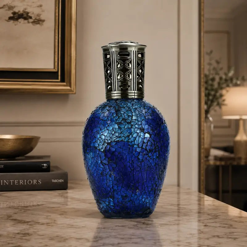 Blue mosaic vase with silver top on a marble surface in an elegant room setting.
