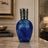 Blue mosaic vase with silver top on a marble surface in an elegant room setting.