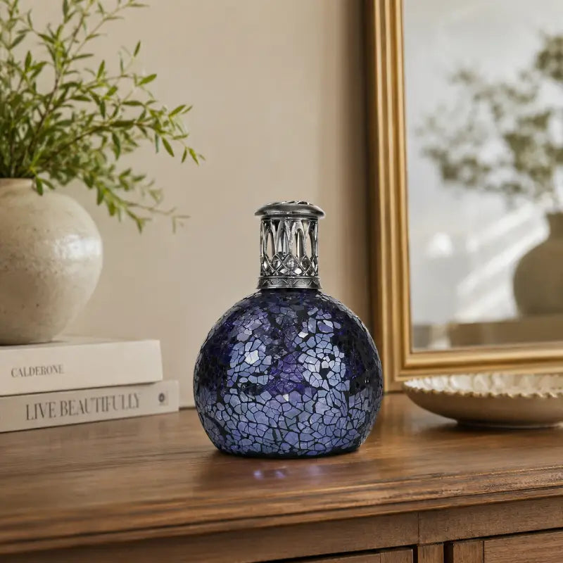 Blue mosaic vase on a wooden surface with a plant and books in the background