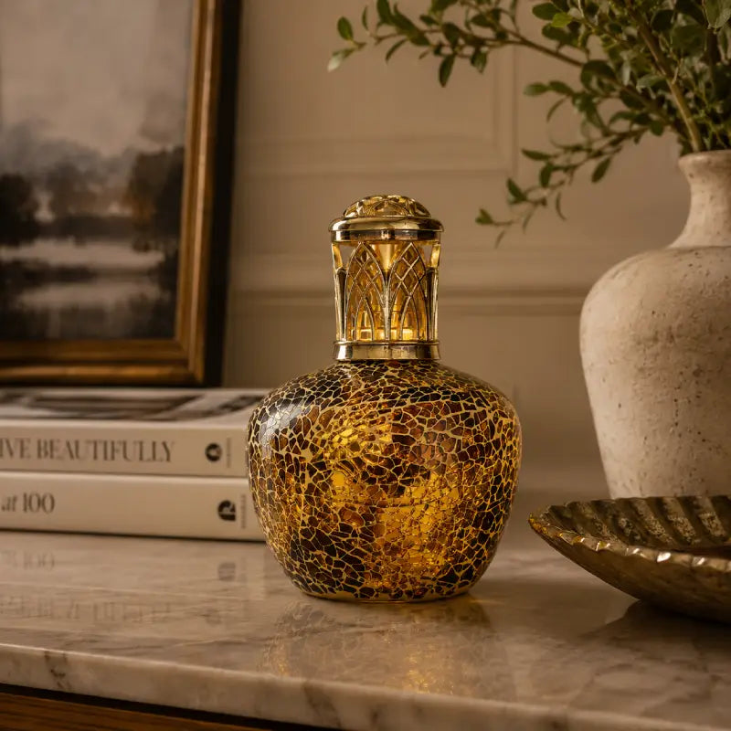 Decorative bottle with intricate design on a marble surface, with books and a vase in the background.