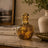 Decorative bottle with intricate design on a marble surface, with books and a vase in the background.