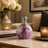 Decorative purple and white mosaic vase on a table with a candle and books in the background.
