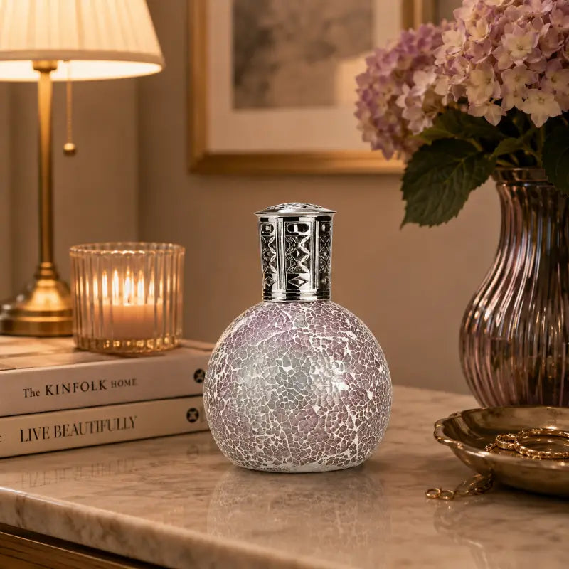 Decorative lamp with crackle glass design on a table with books and flowers.