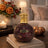 Decorative bottle with mosaic design and gold cap on a table with a cozy background