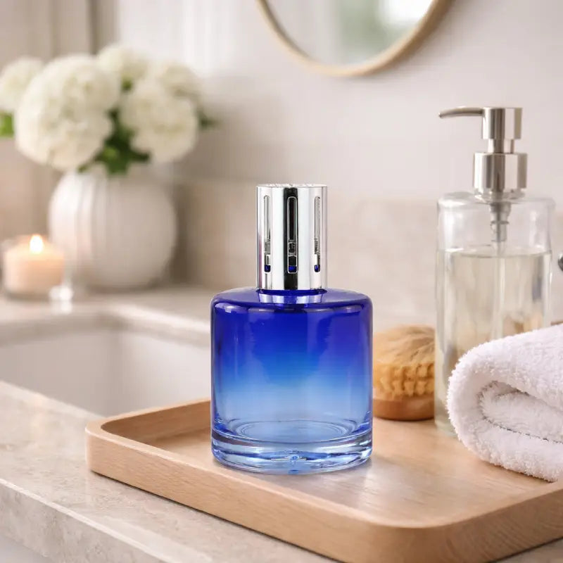 Blue glass bottle with silver cap on a wooden tray in a bathroom setting.