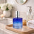 Blue glass bottle with silver cap on a wooden tray in a bathroom setting.