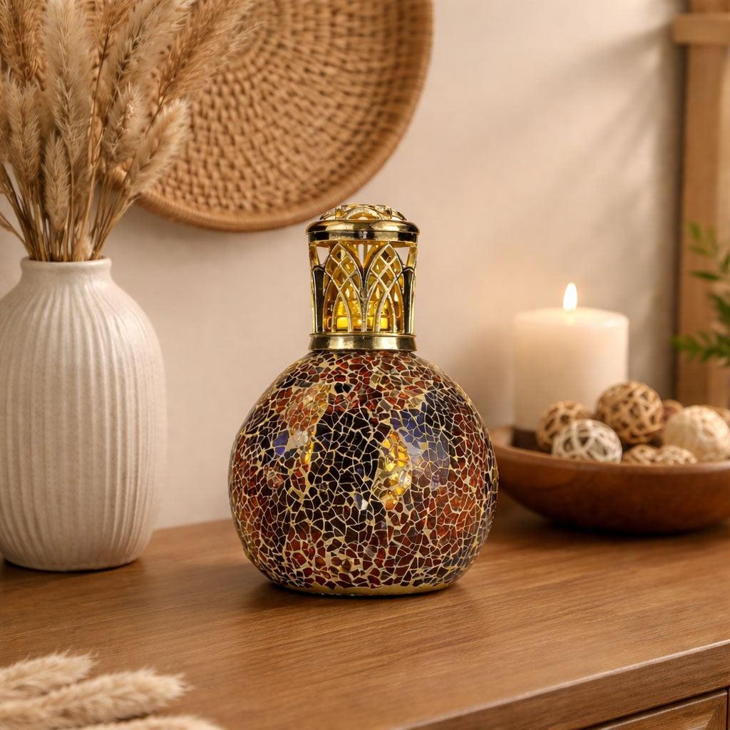Decorative lamp with mosaic design on a wooden surface, surrounded by a vase with dried plants and a candle.