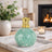 Decorative green vase with gold top on a marble surface in a cozy living room.
