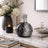 Decorative black and silver vase on a marble surface with books and a candle.