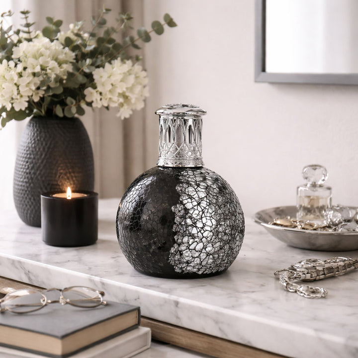 Decorative black and silver vase on a marble surface with books and a candle.