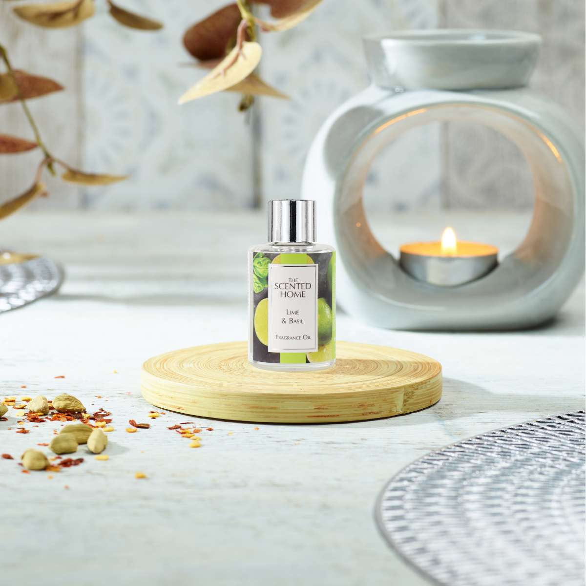A bottle of Lime & Basil Fragrance Oil from The Scented Home Collection on a wooden coaster in front of an Oil Burner