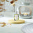 A bottle of Lime & Basil Fragrance Oil from The Scented Home Collection on a wooden coaster in front of an Oil Burner