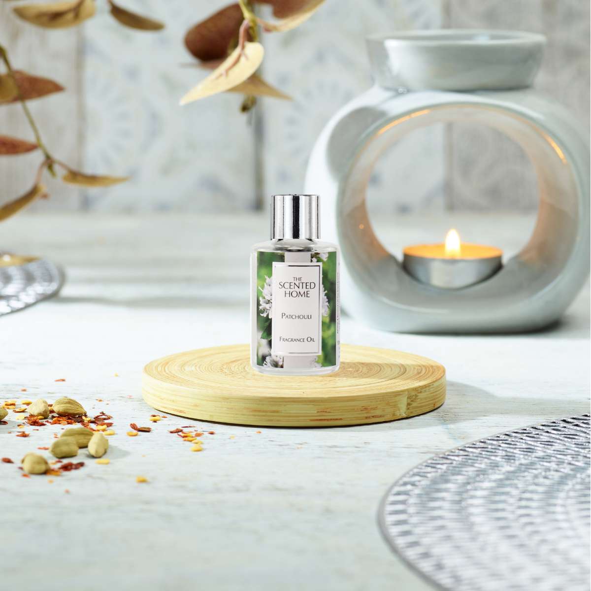 A bottle of Patchouli Fragrance Oil on a wooden coaster with an Oil Burner in the background