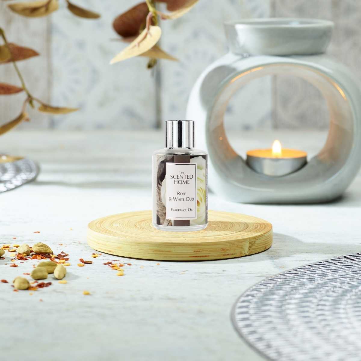 A bottle of Rose & White Oud Fragrance Oil on a wooden coaster infront of an Oil Burner