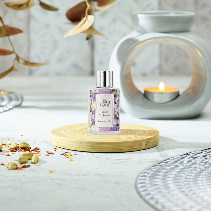 A bottle of Freesia & Orchid Fragrance Oil in the foreground with a burning Oil Burner in the background