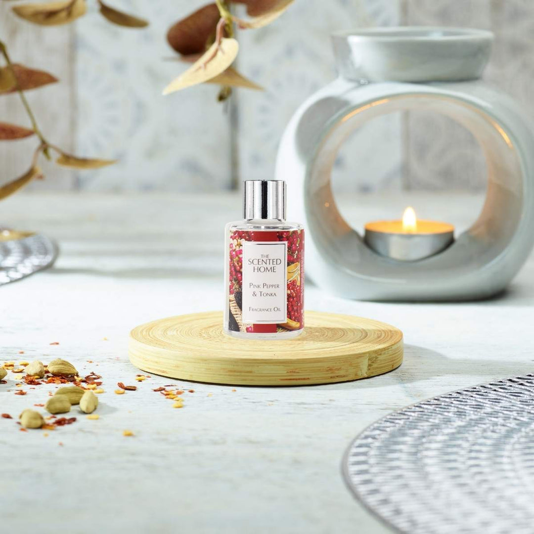 A bottle of Pink Pepper & Tonka Fragrance Oil in the foreground with a burning Oil Burner in the background