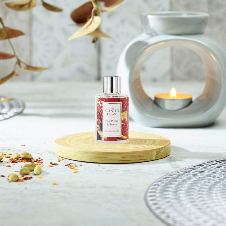 A bottle of Pink Pepper & Tonka Fragrance Oil in the foreground with a burning Oil Burner in the background