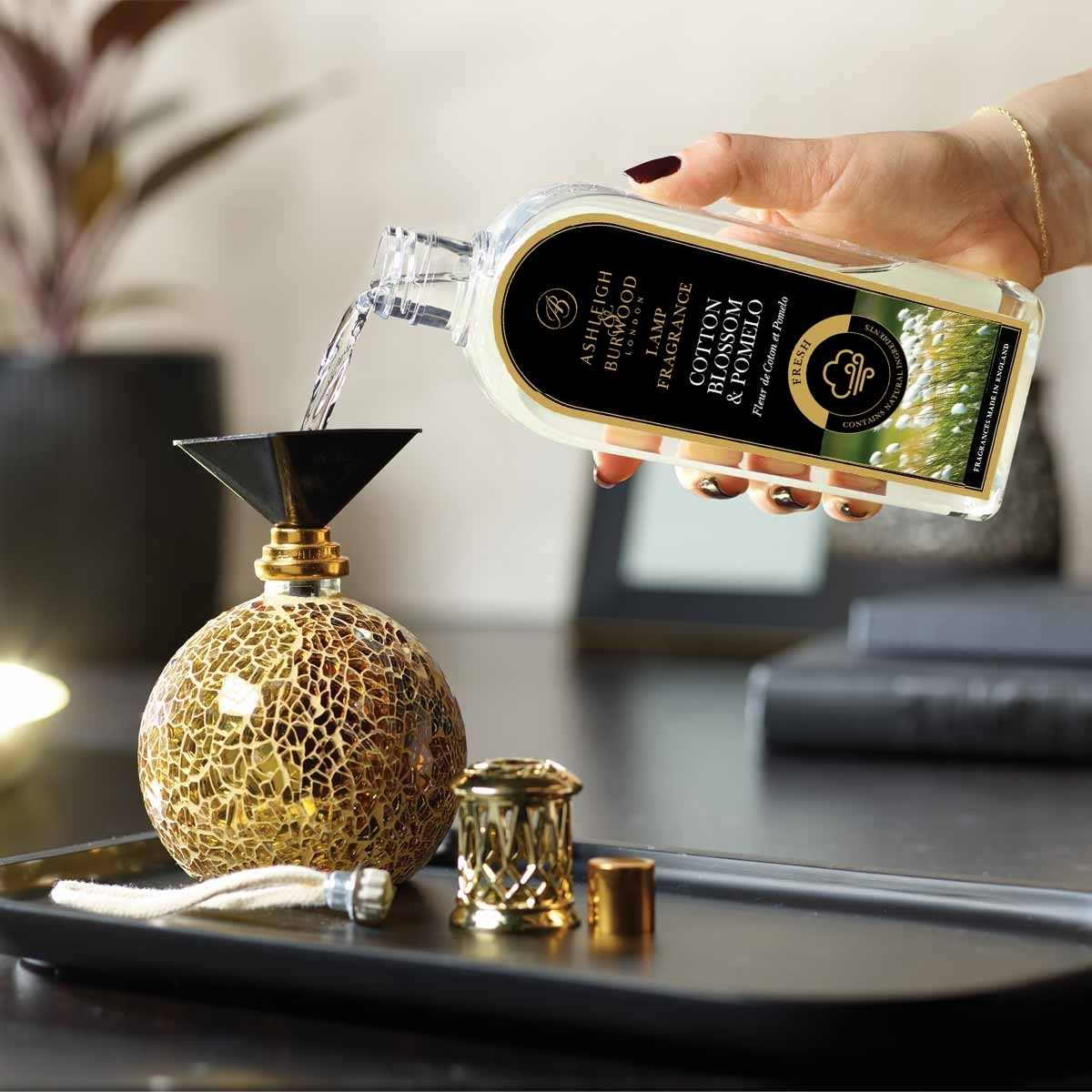 A bottle of Cotton Blossom & Pomelo Lamp Fragrance being poured into a Fragrance Lamp