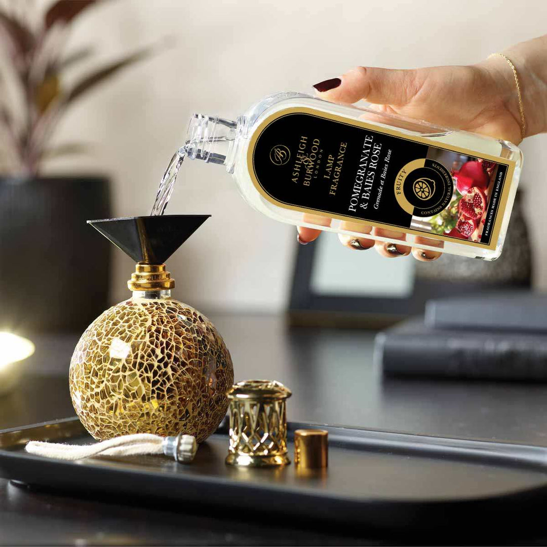A bottle Pomegranate and Baies Rose Lamp Fragrance being poured into a Fragrance lamp